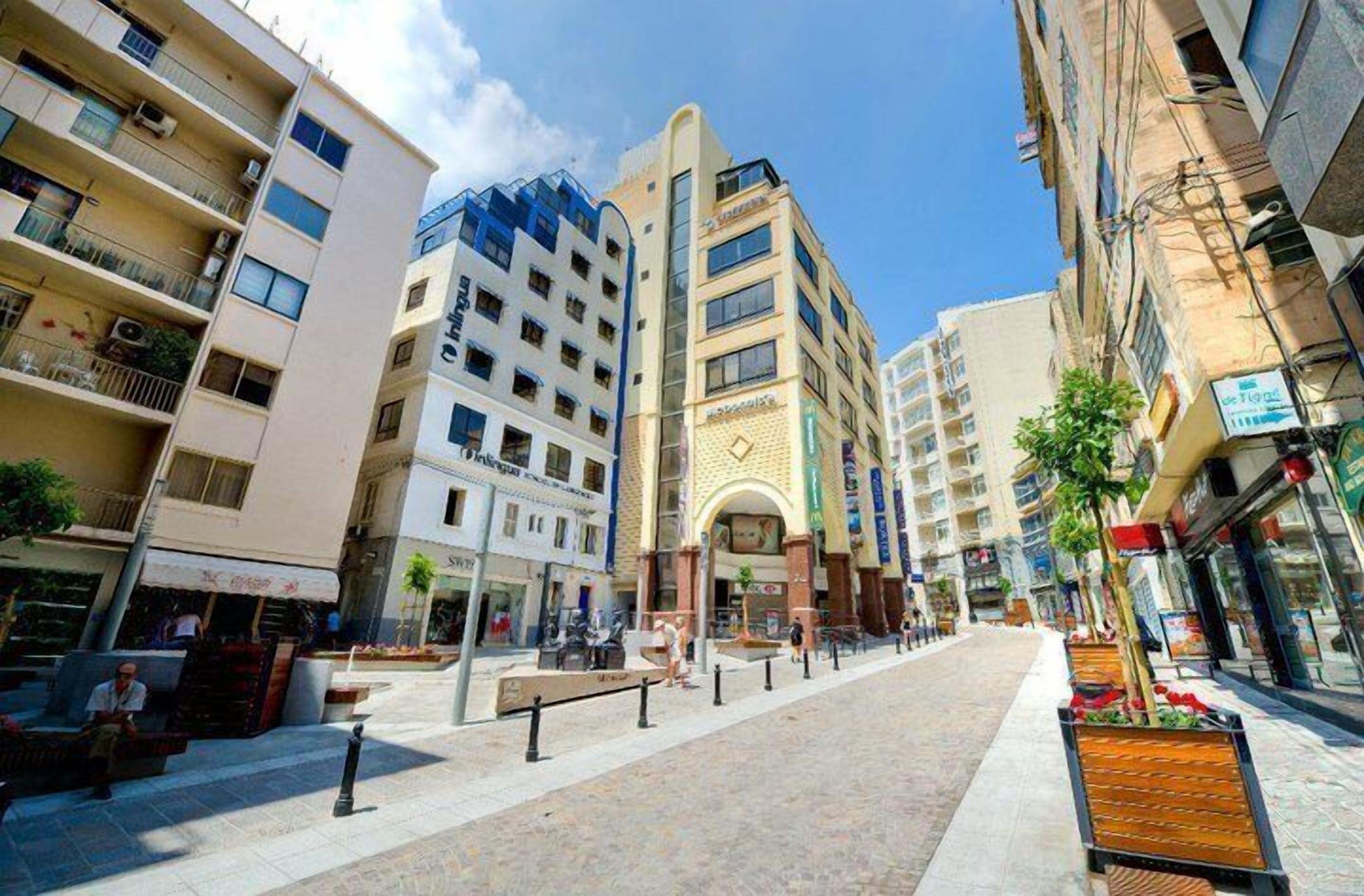 Edifici de diverses plantes amb un pati central, balcons i diferents botigues a la planta baixa.
