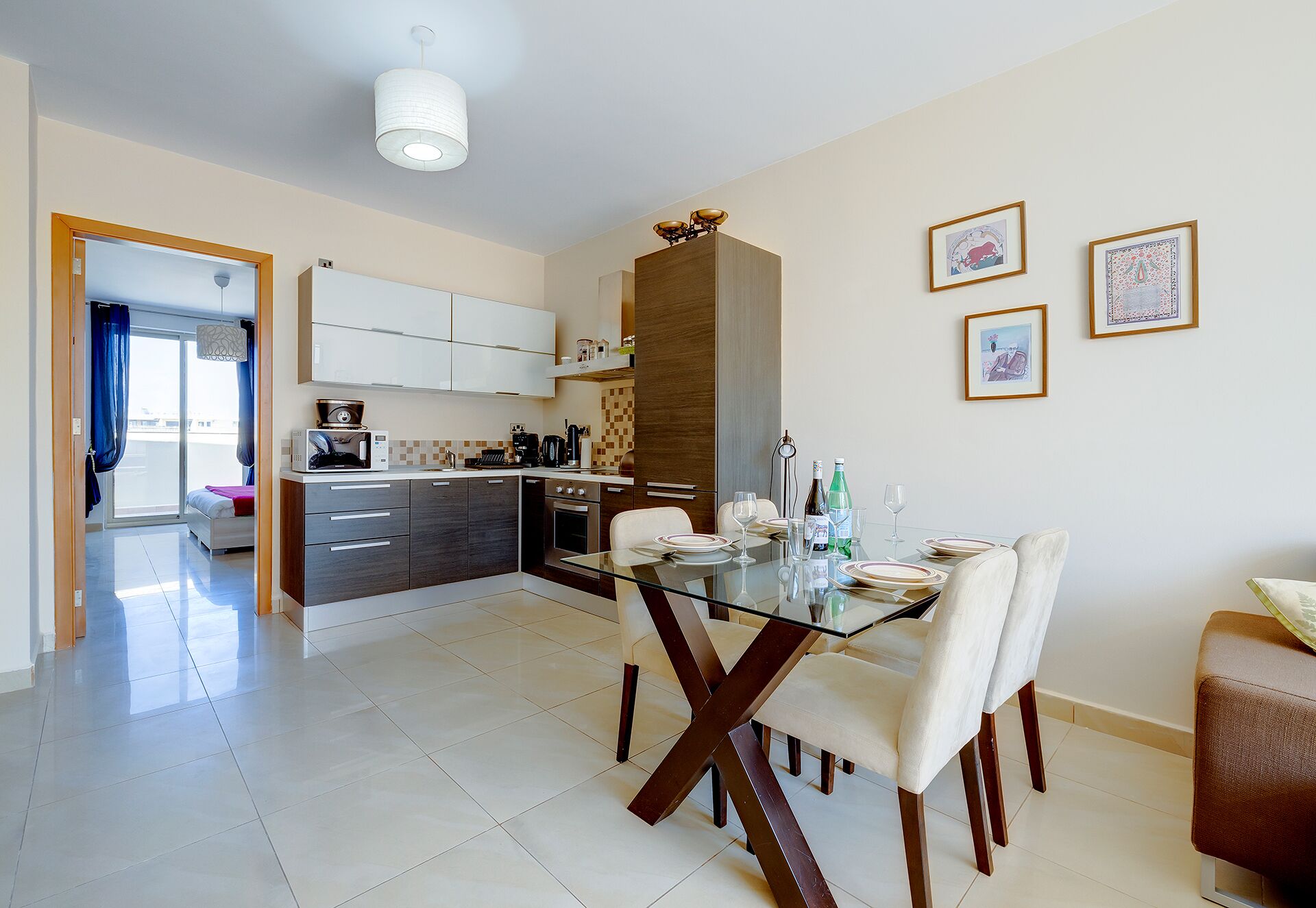 A modern kitchen with white cabinets, a dining area with a glass table, and a view to a balcony.