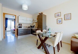 A modern kitchen with white cabinets, a dining area with a glass table, and a view to a balcony. - Cosy 1BR Penthouse Close to the Promenade (Sliema)
