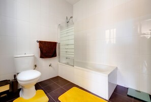 A bathroom with a white toilet, a glass shower enclosure, a bathtub, and two yellow bath mats. - Cosy 1BR Penthouse Close to the Promenade (Sliema)