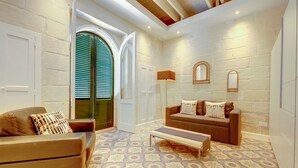 A cozy living room with a patterned floor, a brown sofa, a wooden bench, and a green door with shutters. - Central 1BR Apartment in Valletta (Valletta)