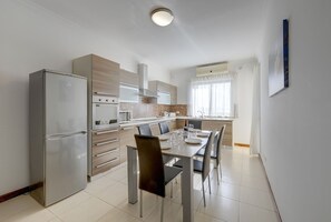 A modern kitchen with a built-in oven, a dining table with chairs, and a large window with curtains. - Modern 3BR Apartment in the Centre of Sliema (Gzira)