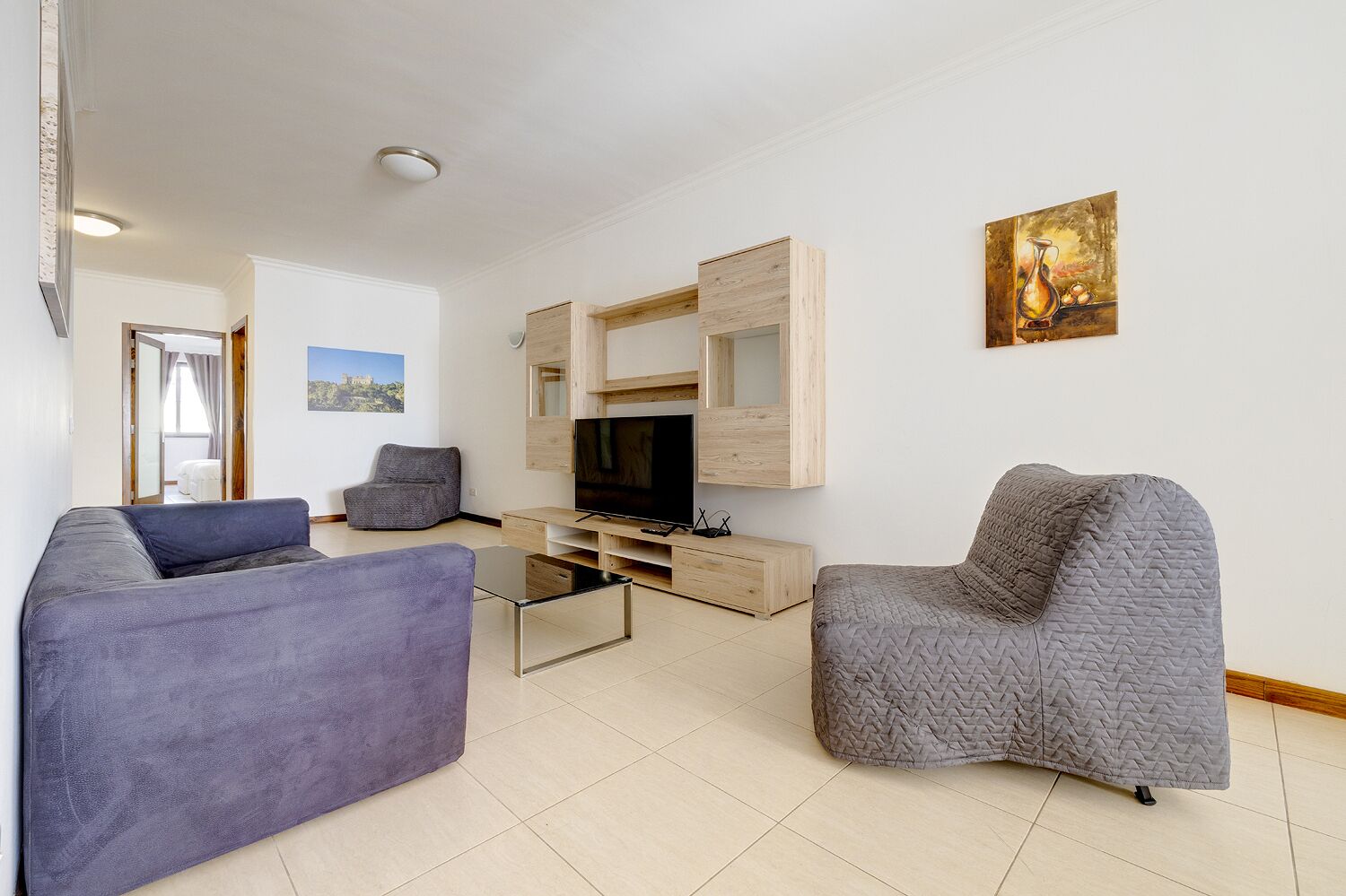 A modern living room with a flat-screen TV, two grey sofas, and a wooden entertainment unit.
