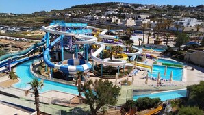 A water park with multiple slides and pools, surrounded by palm trees and a hilly landscape in the background. - Modern 3BR Apartment in the Centre of Sliema (Gzira)
