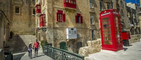 A stone building with red window shutters and a red telephone booth.