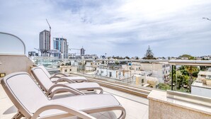 A rooftop terrace with lounge chairs, a view of the cityscape, and a construction crane in the distance. - Marvellous 3BR Penthouse in Central St Julian's (Swieqi)