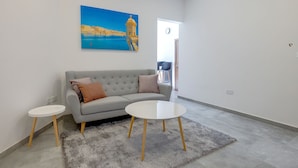 Uma sala de estar moderna com um sofá cinza, duas mesinhas de cabeceira brancas e um tapete felpudo cinza.