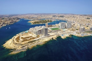An aerial view of a coastal city with a prominent marina, high-rise buildings, and a sandy beach area. - Perfect Location, Modern 2BR Apartment (Sliema)