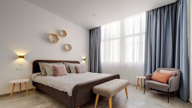 Quarto moderno com uma cama grande, um banco, uma cadeira e uma mesa pequena.