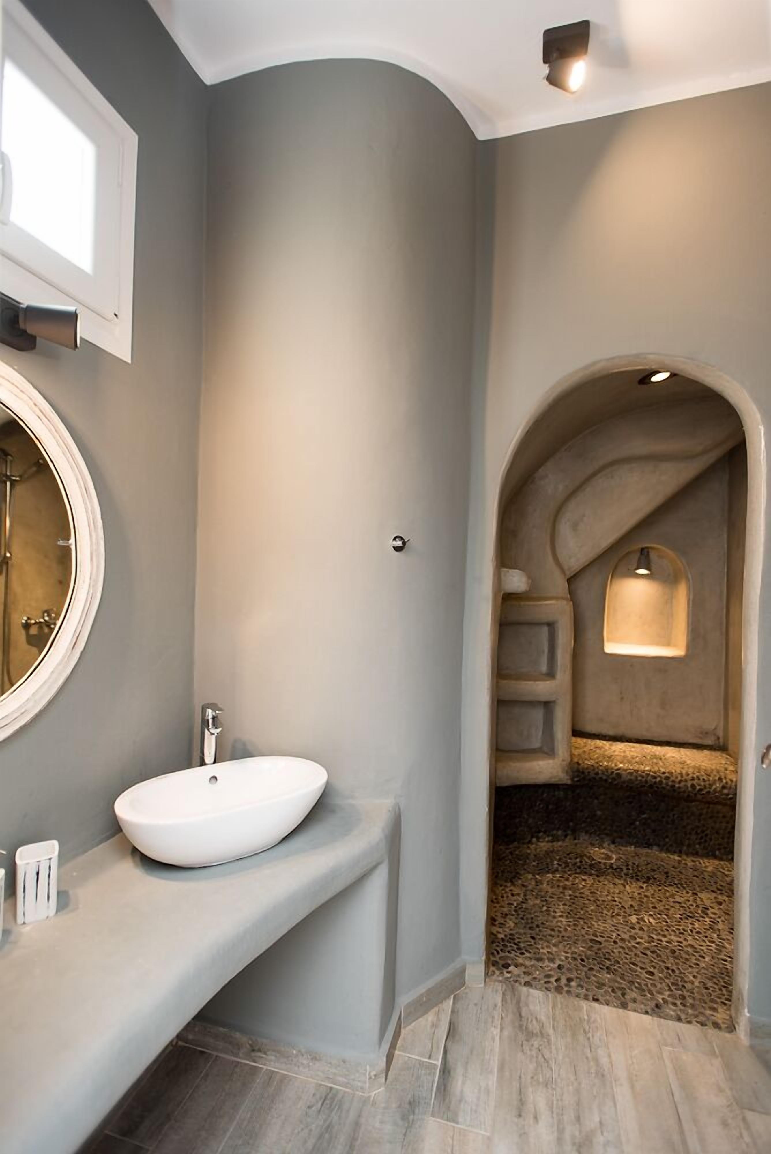 A modern bathroom with a curved vanity, a round mirror, and a built-in shower area with a stone wall.