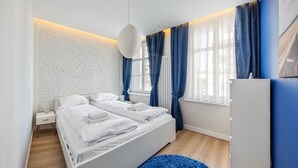 Een moderne slaapkamer met een witte baksteenmuur, een wit bed, blauwe gordijnen en een blauw vloerkleed.