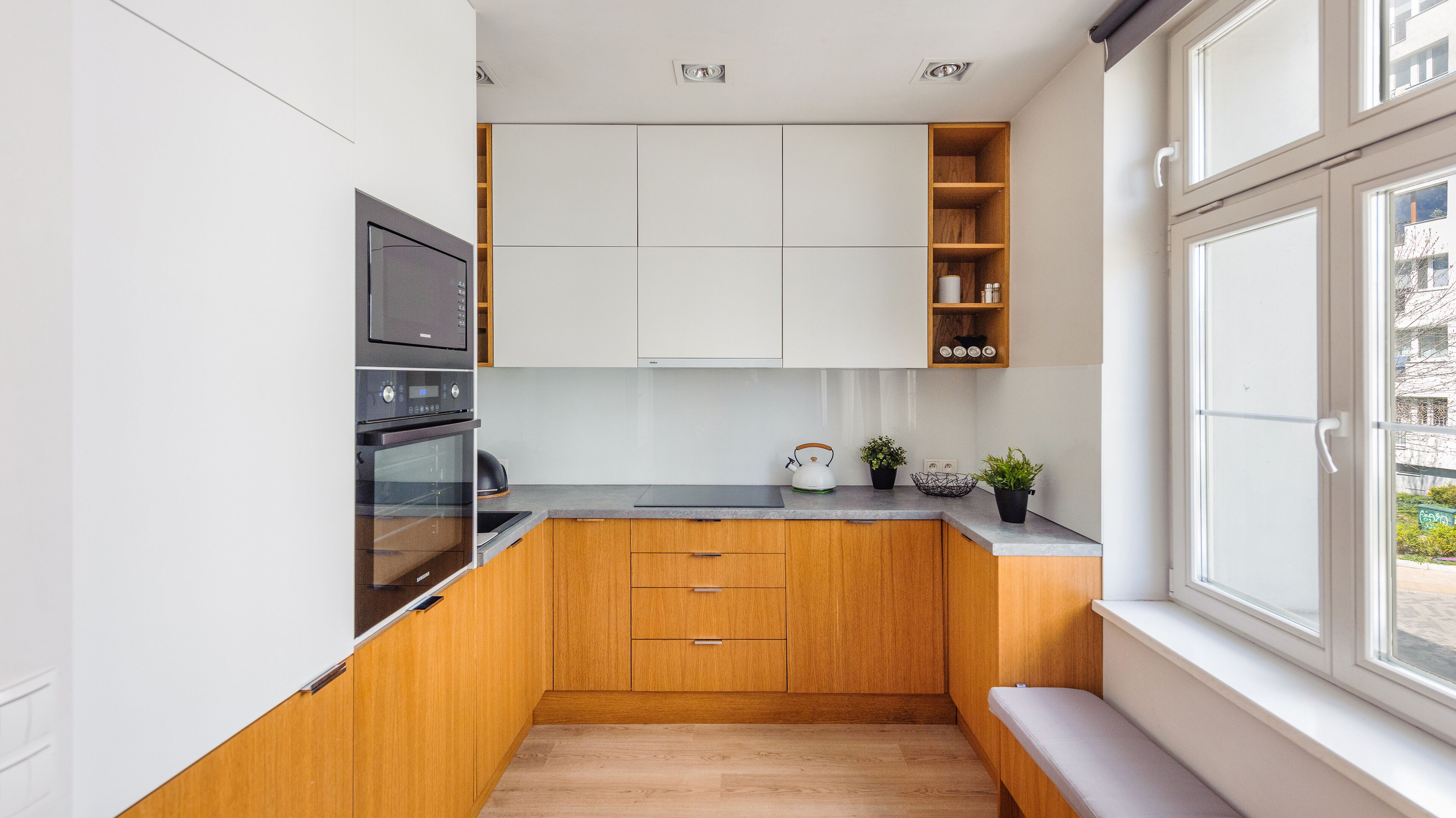 A compact kitchen with wooden cabinets, a built-in oven, and a window with a view of the outside.