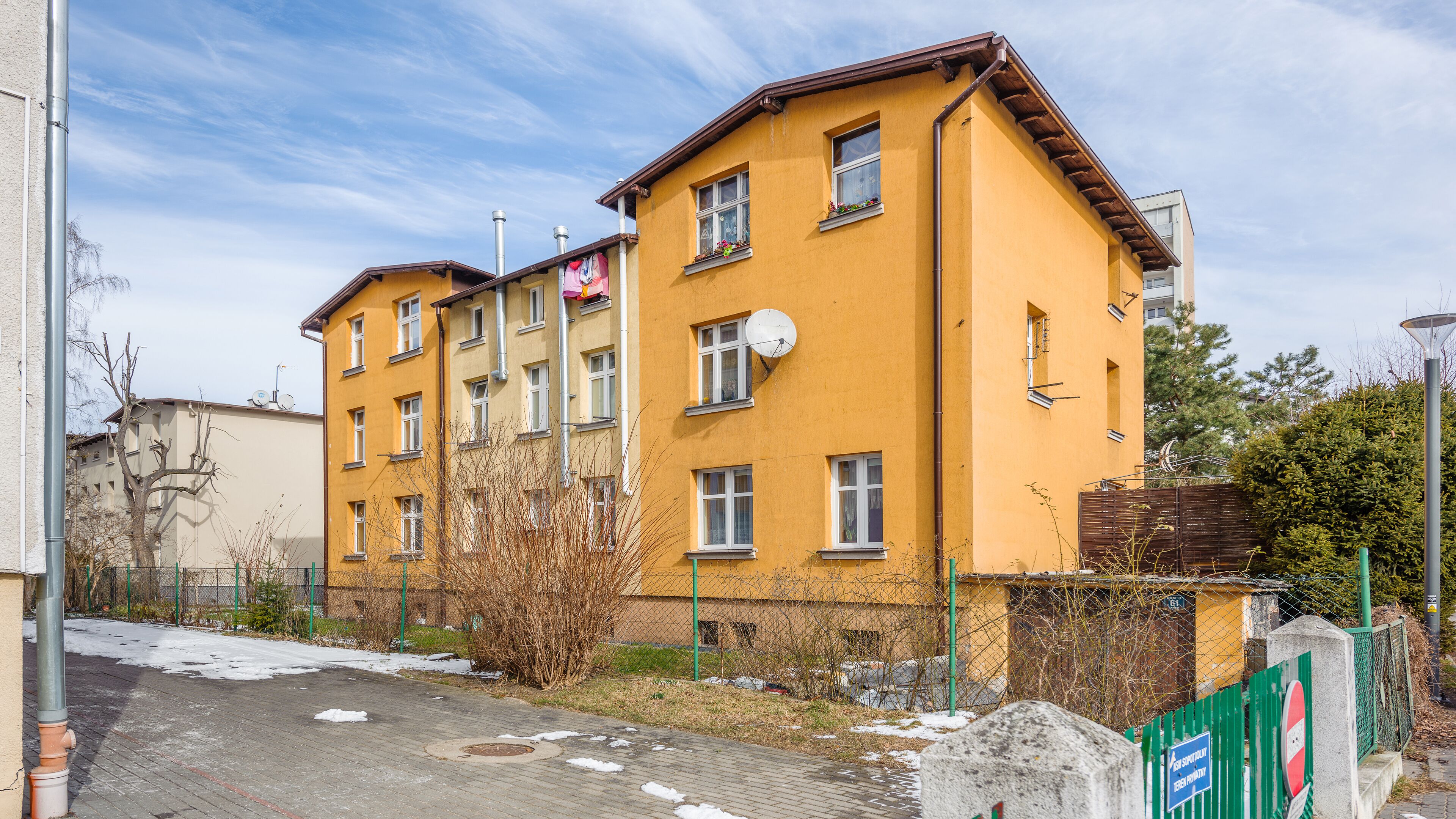A multi-story yellow building with multiple windows, a satellite dish, and a green fence.