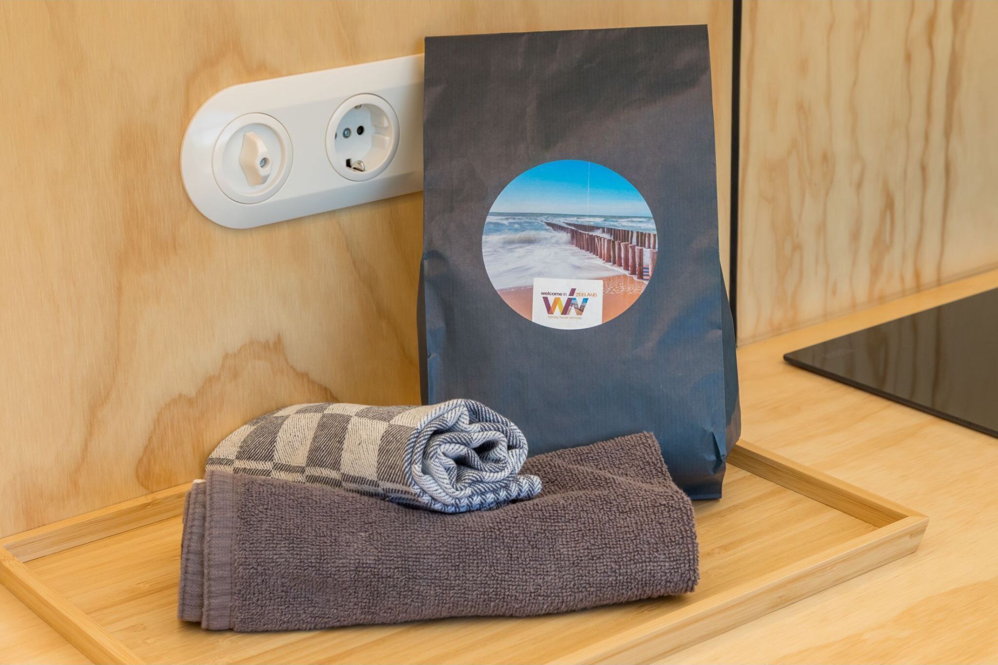 Een houten dienblad met een opgevouwen handdoek en een tas met een kustlandschap.