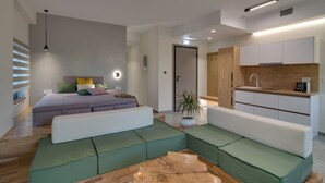 A modern living room with a sectional sofa, a coffee table, and a small kitchen area with white cabinets and a wooden countertop. - Selin Luxury Residences (Ioannina)