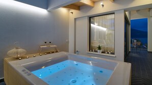 A modern bathroom with a large bathtub, a window with curtains, and a small table with candles. - Selin Luxury Residences (Ioannina)