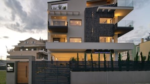 A modern multi-story residential building with balconies, a gated entrance, and a well-maintained garden. - Selin Luxury Residences (Ioannina)