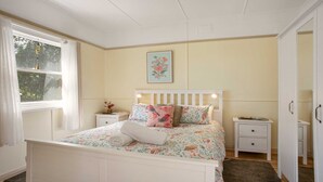 Une chambre à coucher comprenant un lit, des tables de chevet, une armoire et une fenêtre avec des rideaux.