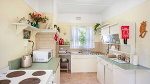 Une cuisine compacte équipée d’une cuisinière, d’un four à micro-ondes, d’un évier et de divers appareils électroménagers. On y trouve des étagères remplies d’objets et une fenêtre avec des rideaux.