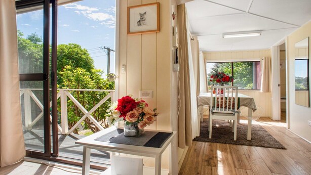 Une pièce avec un balcon, une table ornée d’un vase de fleurs, une chaise et un lit à l’arrière-plan.