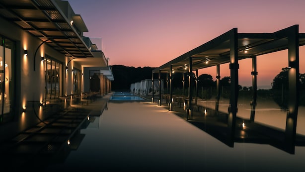 Un hotel modern amb zona de piscina, seients coberts i vistes al capvespre.