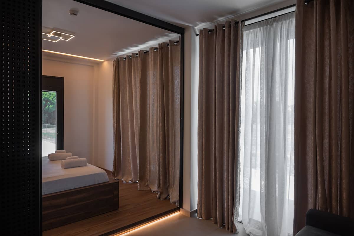 Un dormitorio moderno con una cama grande, una plataforma de madera y vistas a la vegetación exterior.