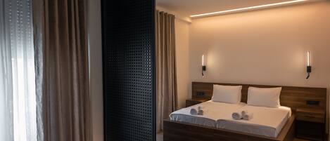 A modern hotel room with a wooden bed, two bedside tables, a large mirror, and a wall-mounted light fixture.