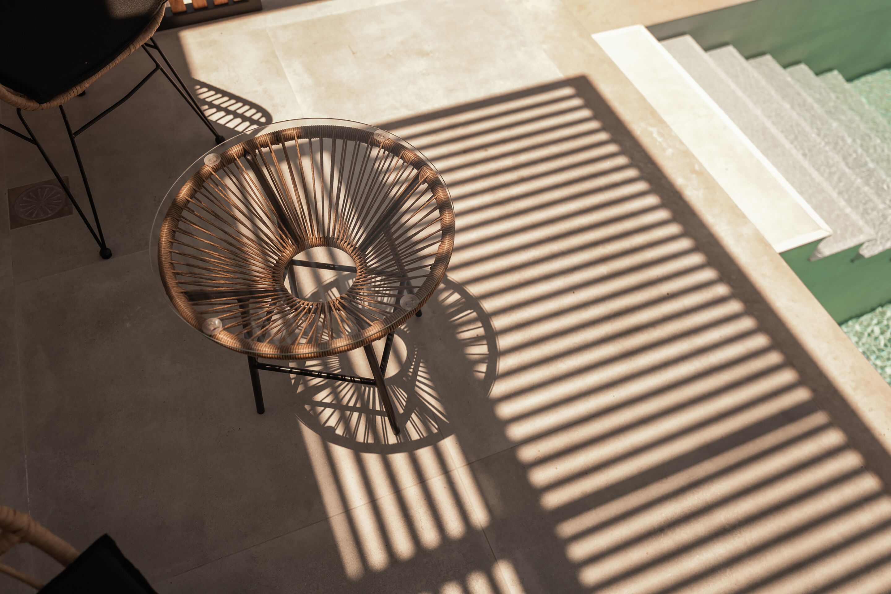 A wicker chair with a circular design and a metal frame, positioned on a tiled floor with a shadow cast by a nearby object.