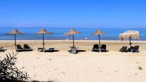Una platja amb cinc sombrerets de palla i gandules, un cel blau clar i mar tranquil·la.