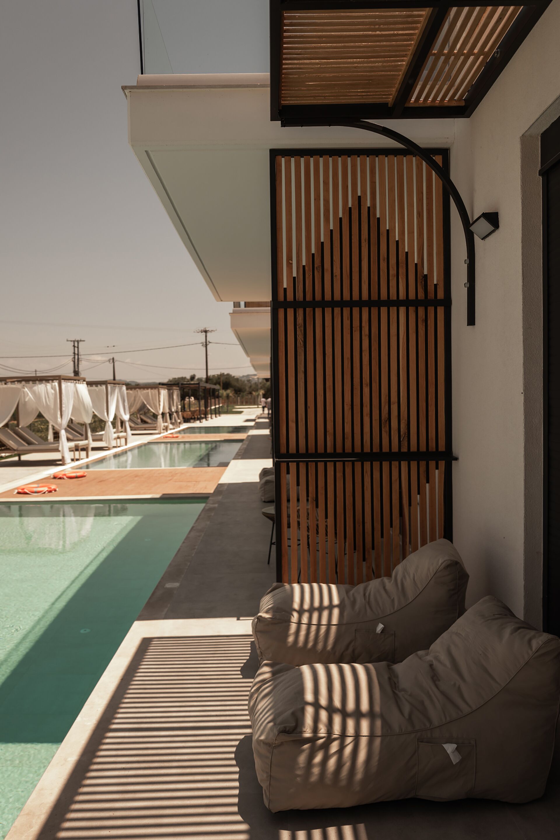 A poolside area with a modern design, including a wooden partition, two beige lounge chairs, and a clear view of the pool.