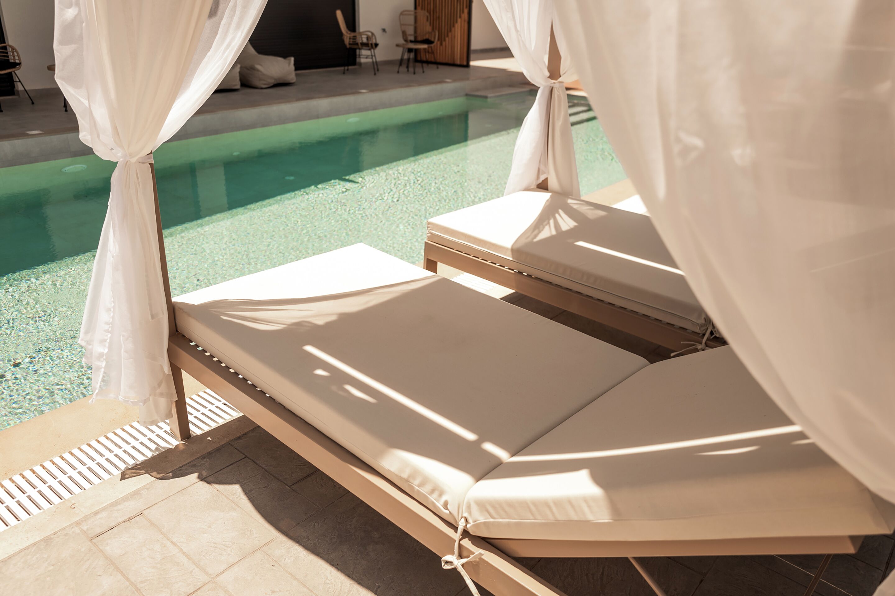 Zona junto a la piscina con dos tumbonas, una piscina cristalina y una zona de estar cubierta.