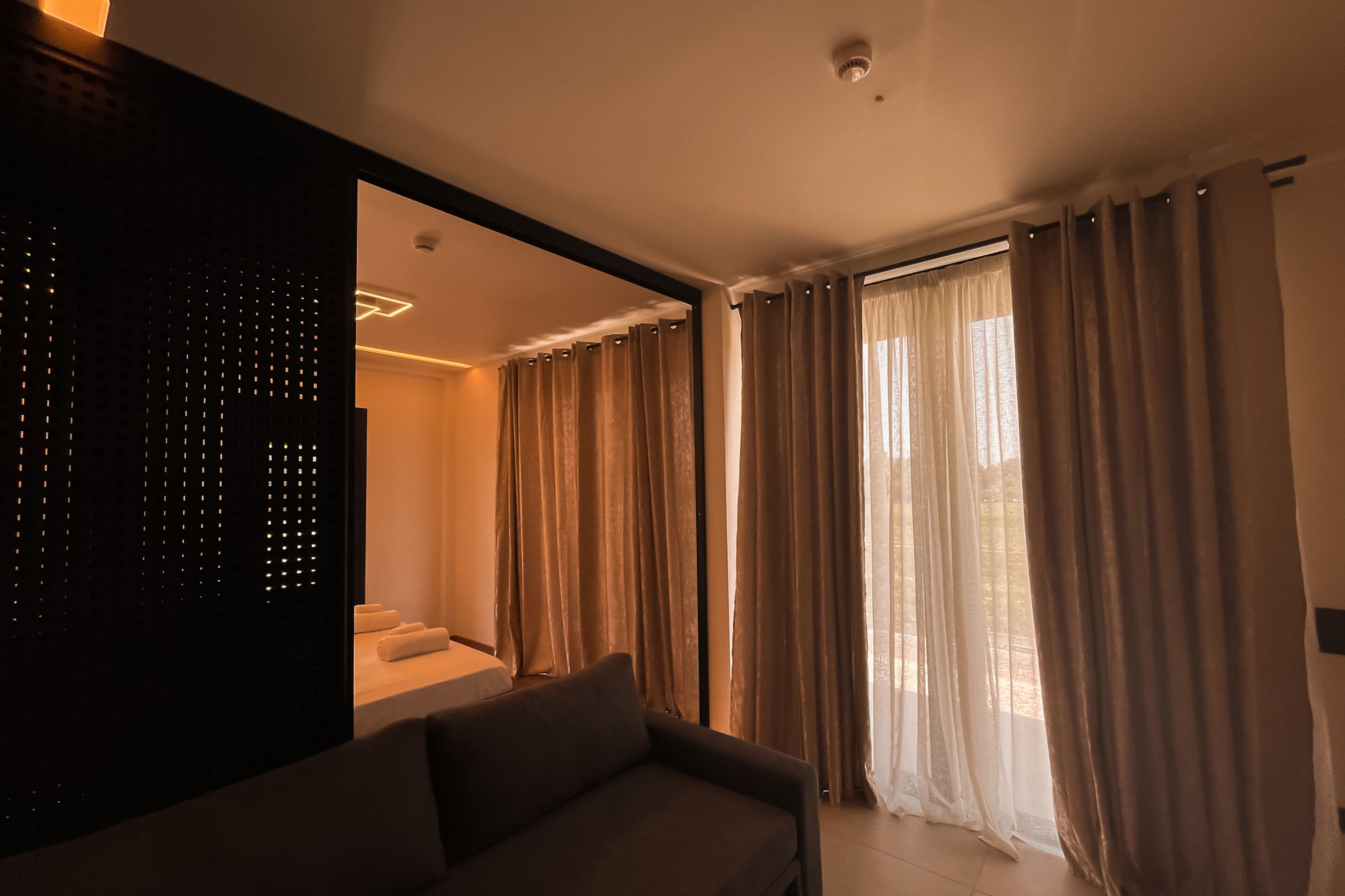 A modern living room with a sofa, a staircase, and large windows with curtains.