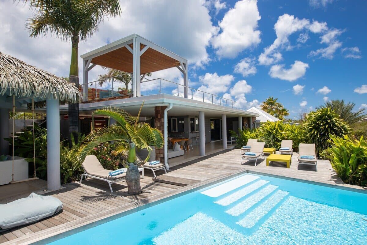 Una villa moderna con piscina, zona de estar exterior y exuberante vegetación.
