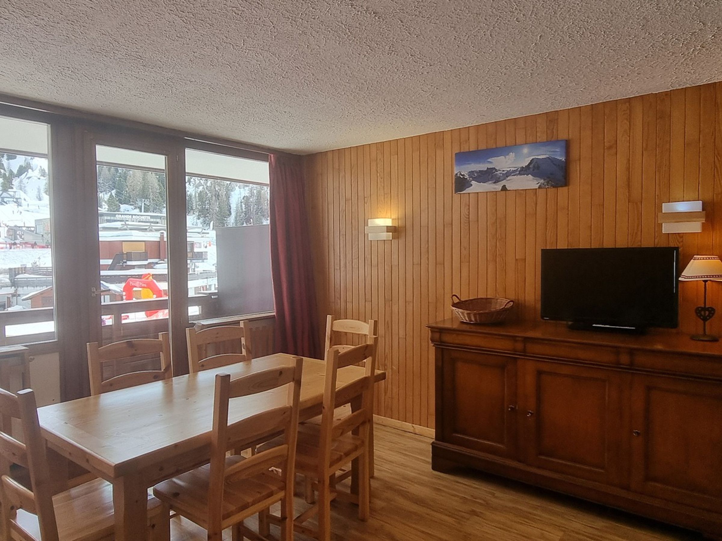 Et rum med træpaneler, et spisebord med stole, et fjernsyn og et maleri på væggen.