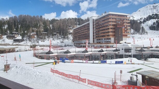 Un hotel con diversi piani, una località sciistica sullo sfondo e un paesaggio innevato.