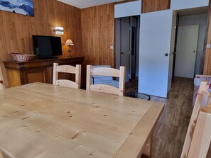 Een kamer met houten lambrisering, een eettafel, stoelen, een televisie en een lamp.