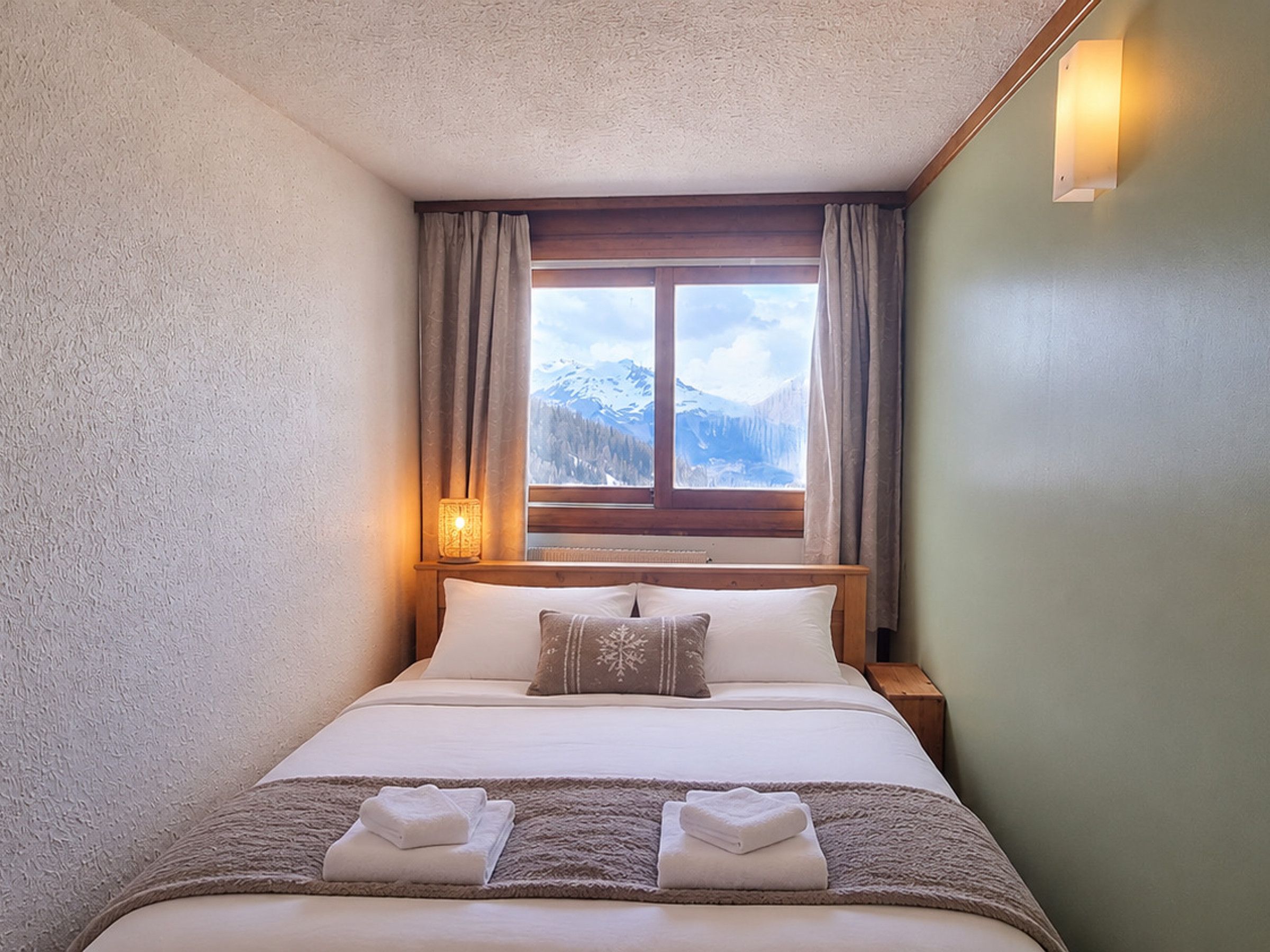 A hotel room with a bed, a window with curtains, a nightstand, and a lamp.