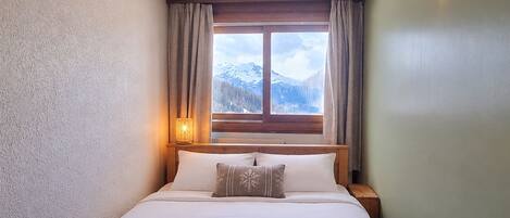 A hotel room with a bed, a window with curtains, a nightstand, and a lamp.