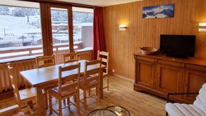 Una stanza con rivestimenti in legno, un tavolo da pranzo, sedie, un televisore e vista su un paesaggio innevato attraverso ampie finestre.