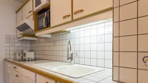 Una cucina con piastrelle bianche, un lavello doppio, mobili in legno e un forno a microonde.