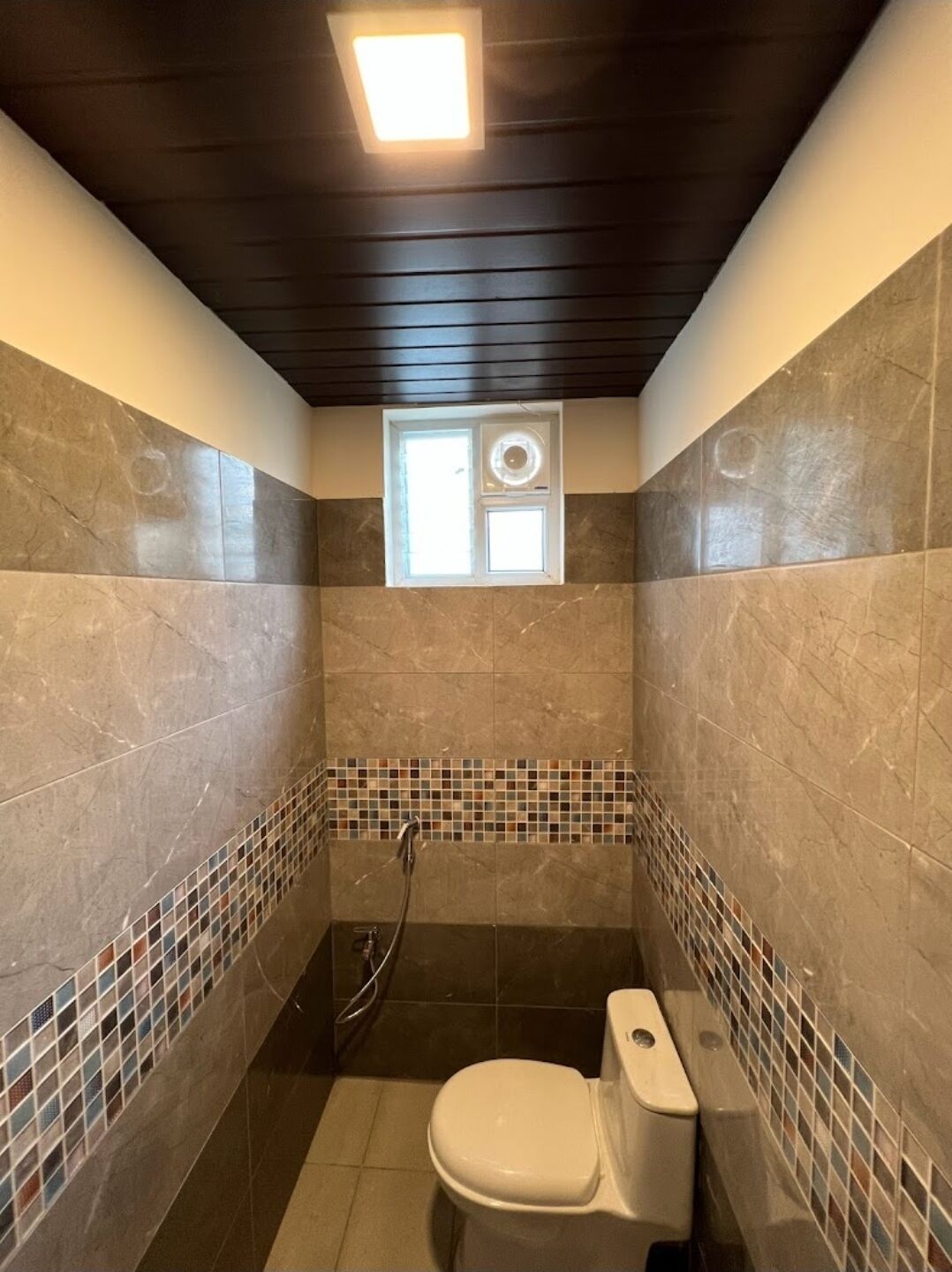 Ein kleines Badezimmer mit Toilette, Dusche und Fenster.