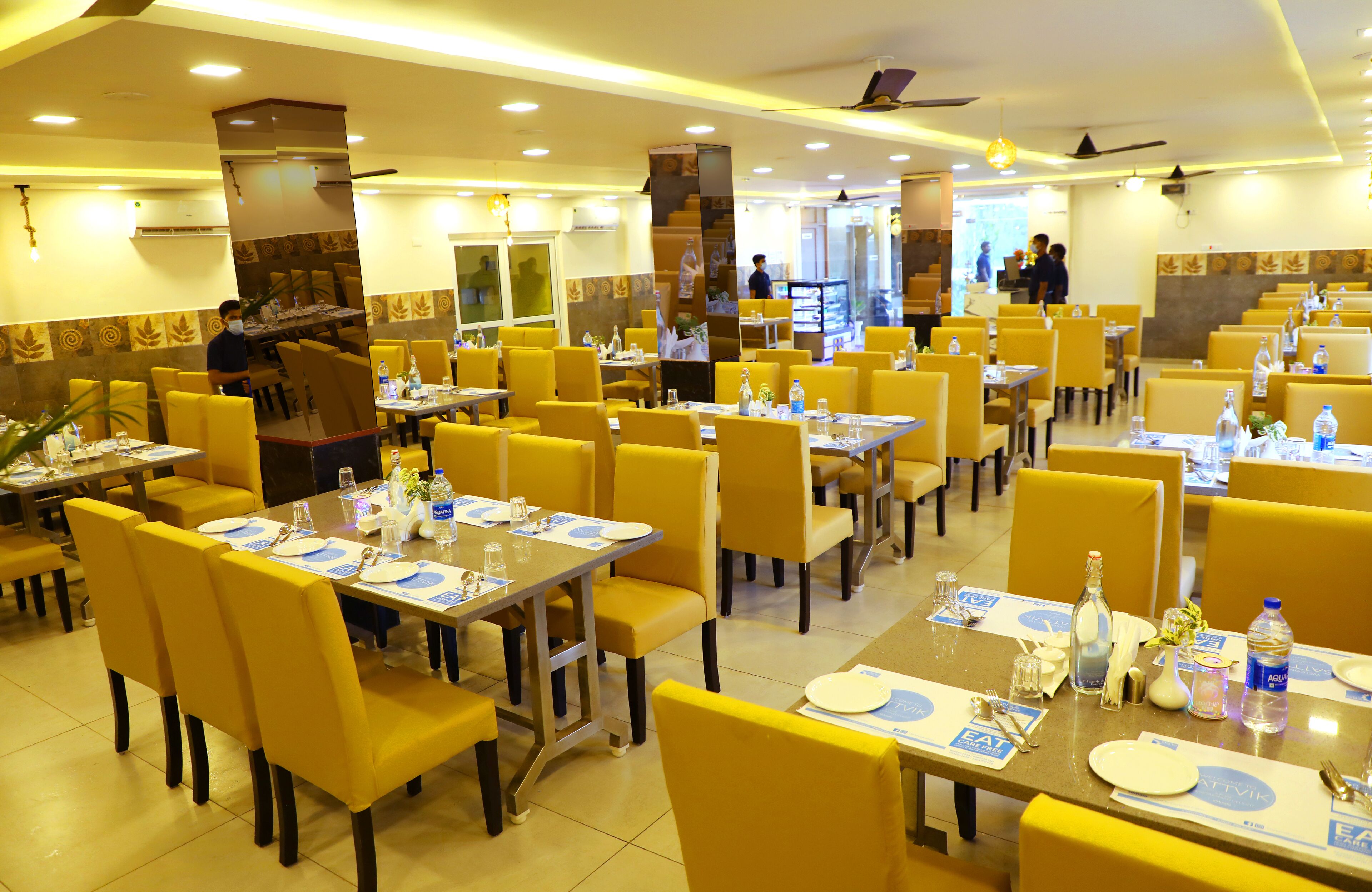 A restaurant with yellow chairs and tables, some with water bottles and glasses.