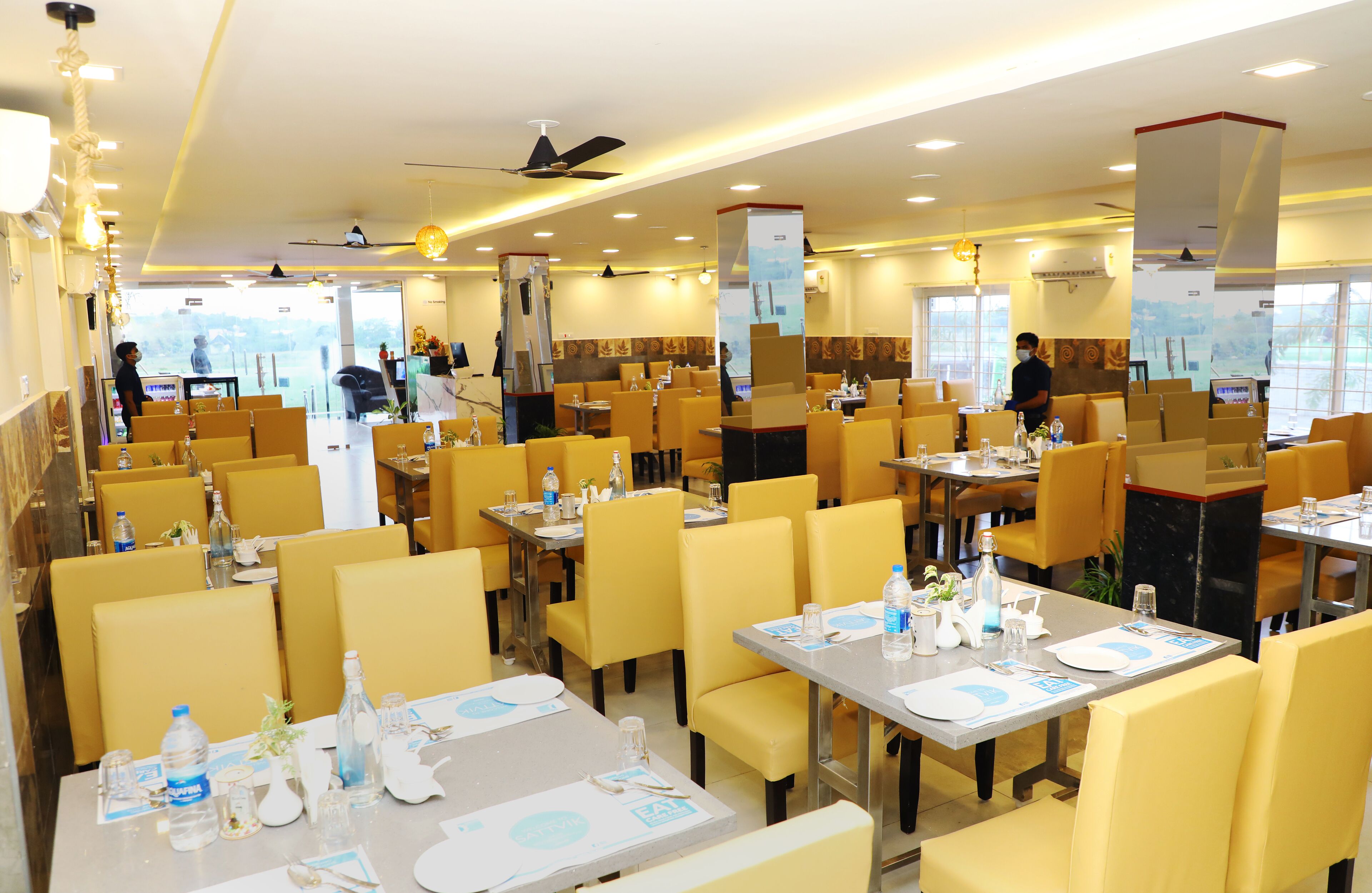 A spacious restaurant with yellow chairs and tables, equipped with water bottles and menus.