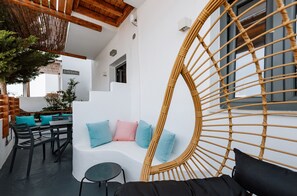 A modern outdoor seating area with a white cushioned bench, a wicker chair, and a small round table. - Piperaki Project Paros (Paros)