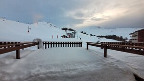 Ein mit Schnee bedeckter Skipisten mit Holzbanken und einer Seilbahn im Hintergrund.