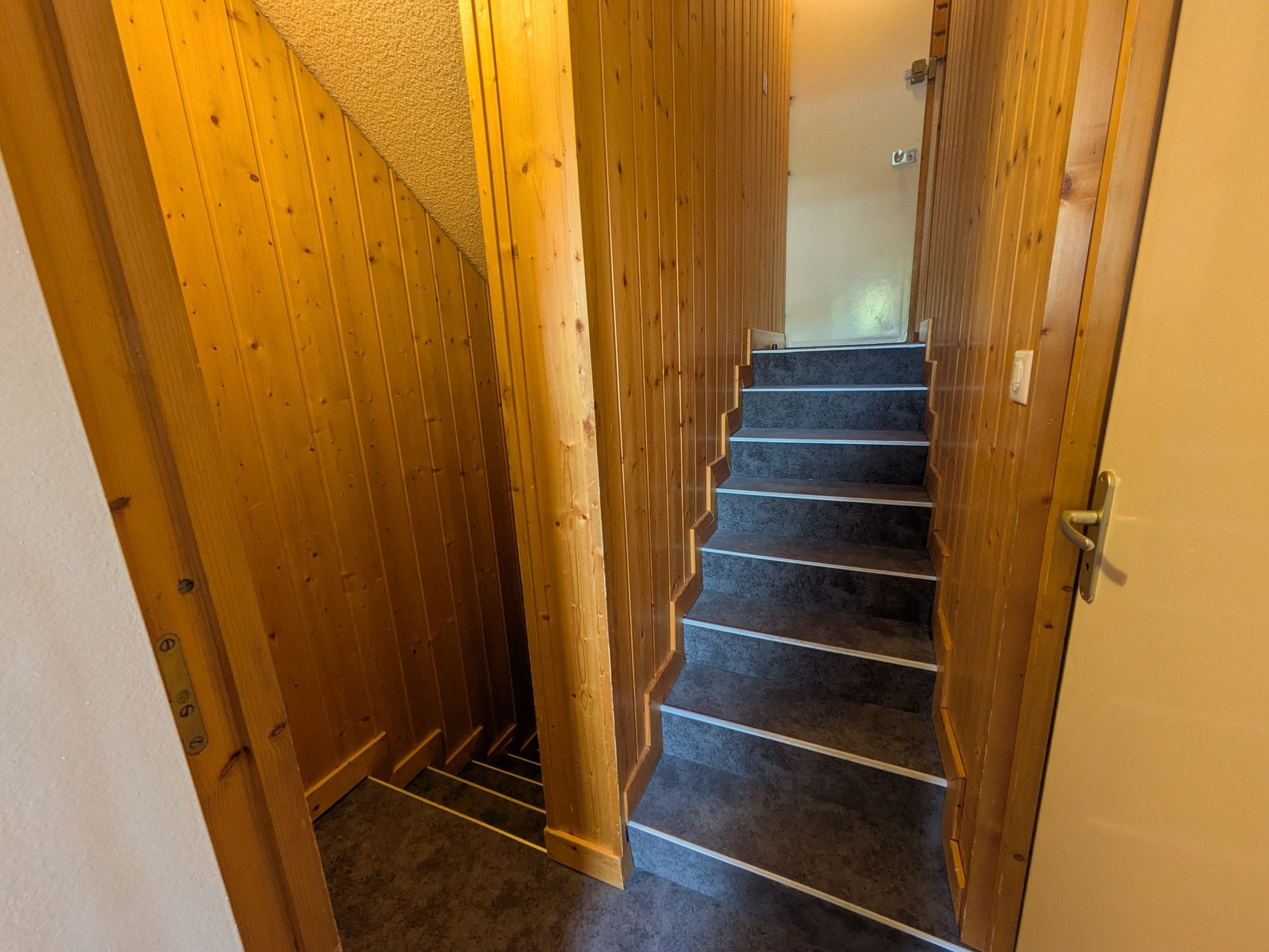 Una escalera de madera con peldaños alfombrados que conduce a una habitación con una puerta blanca.