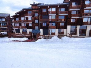 A multi-story wooden building with balconies, a covered outdoor seating area, and a snow-covered ground. - Duplex Apartment 2 Rooms · Ski-in/Ski-out · Terrace (Plagne Villages)