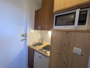 A compact kitchen with wooden cabinets, a built-in microwave, a sink, and a compact refrigerator.