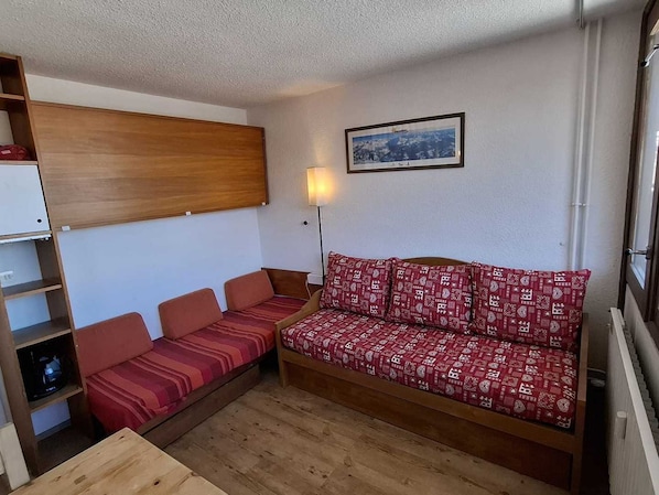 A compact room with a sofa bed, a small table, and a wall-mounted shelf.
