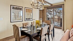 A dining area with a large table set for six, surrounded by chairs, a chandelier, and framed artwork on the walls.